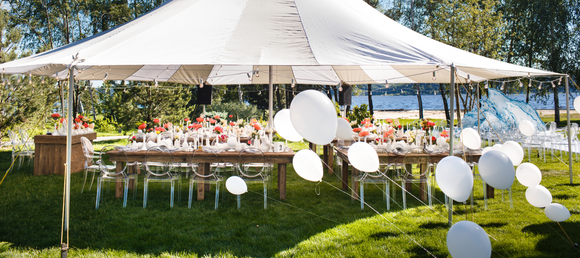 A white party tent with banquet tables and white balloons.