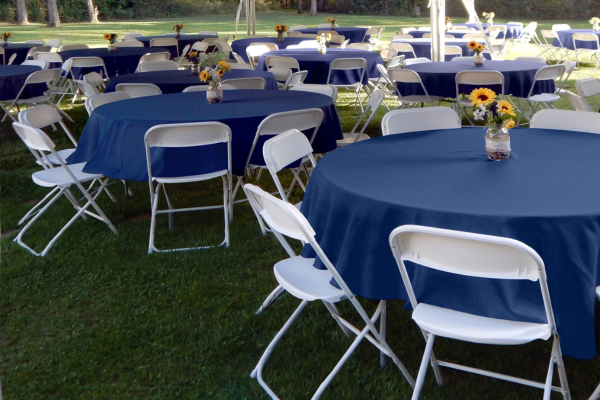 Round tables and chairs set up underneath and event tent outdoors.